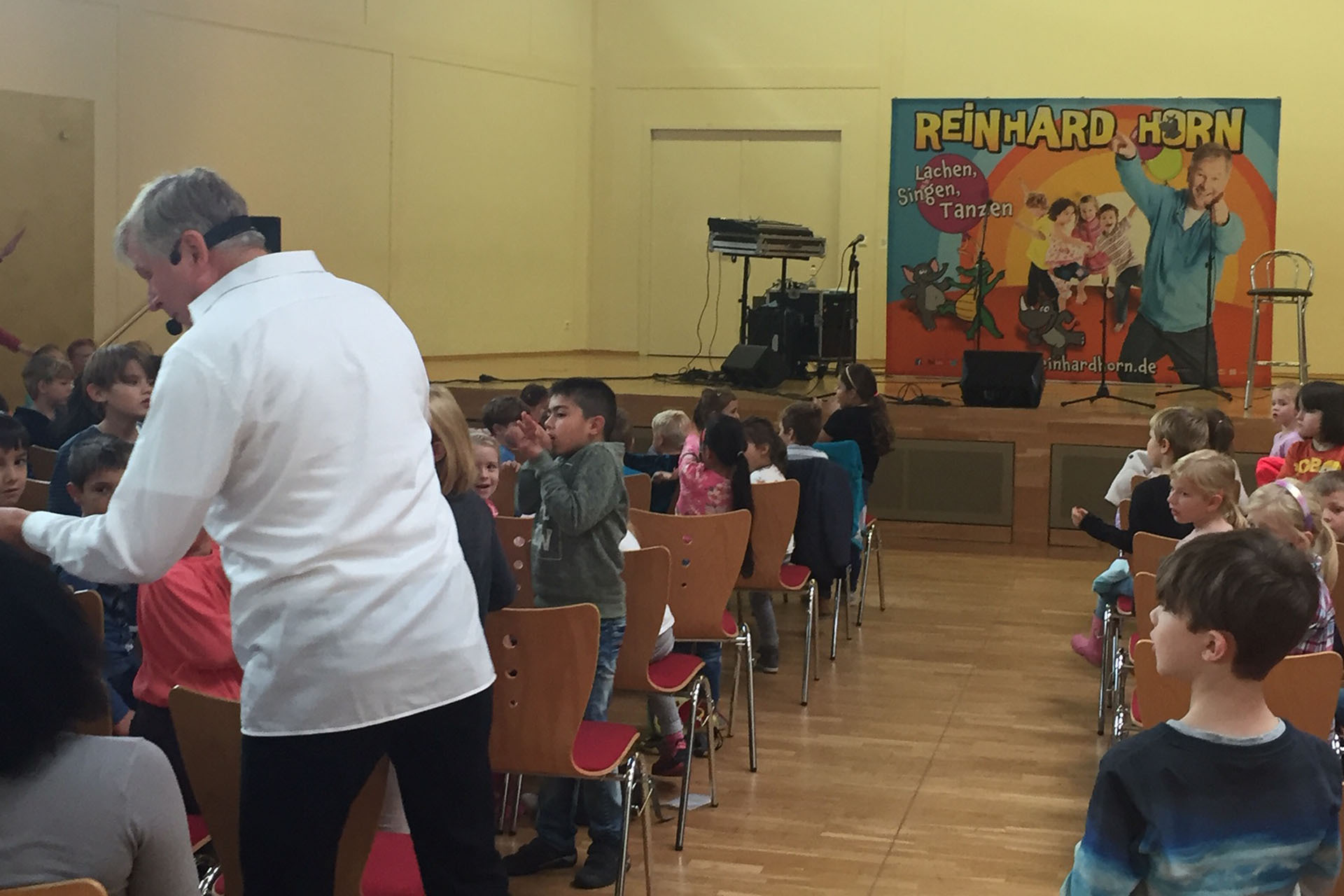 Kinder und ein Erwachsener nehmen an einer Veranstaltung mit dem Künstler Reinhard Horn teil, die Lachen, Singen und Tanzen fördert – Teil eines VIDETO-Projekts zur Stärkung demokratischer Werte und sozialer Integration.