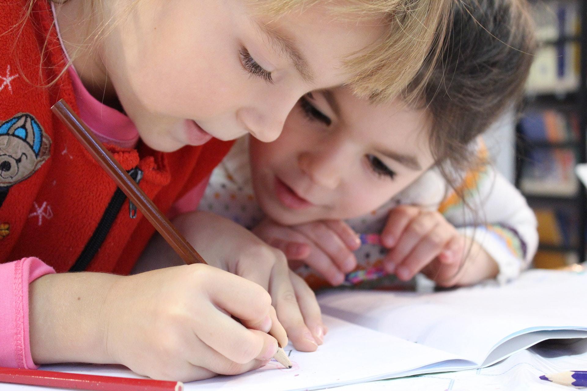 Zwei Kinder zeichnen konzentriert in einem Heft, was die Förderung von Kreativität und demokratischem Miteinander im Rahmen von VIDETO-Projekten für Kinder symbolisiert.
