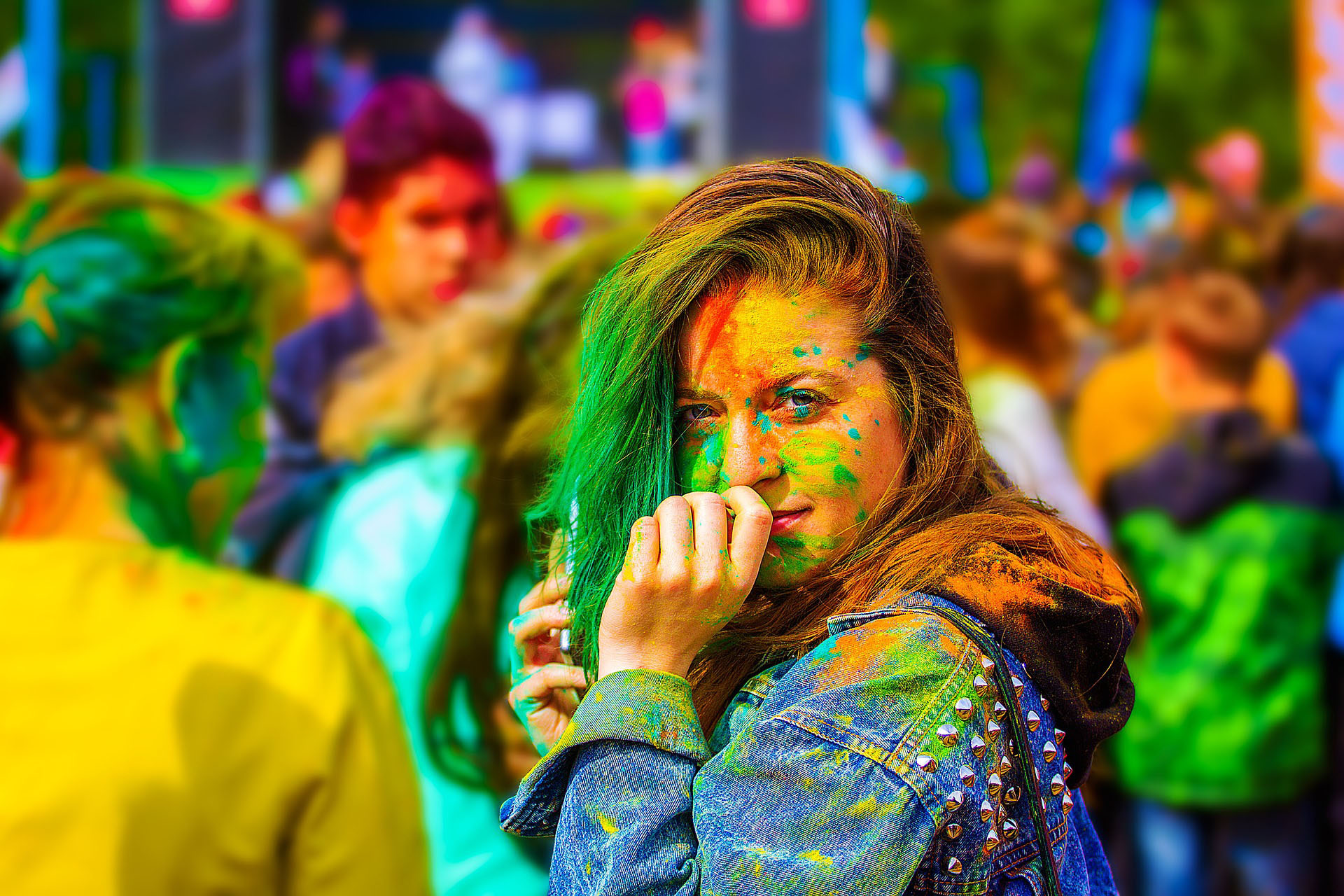 Eine junge Frau mit grünem, orangefarbenem und gelbem Farbpulver im Gesicht und Haaren steht auf einem Festival der Farben, umgeben von anderen Teilnehmern – ein Symbol für Vielfalt, Toleranz und gemeinsames Feiern, das VIDETO fördert.