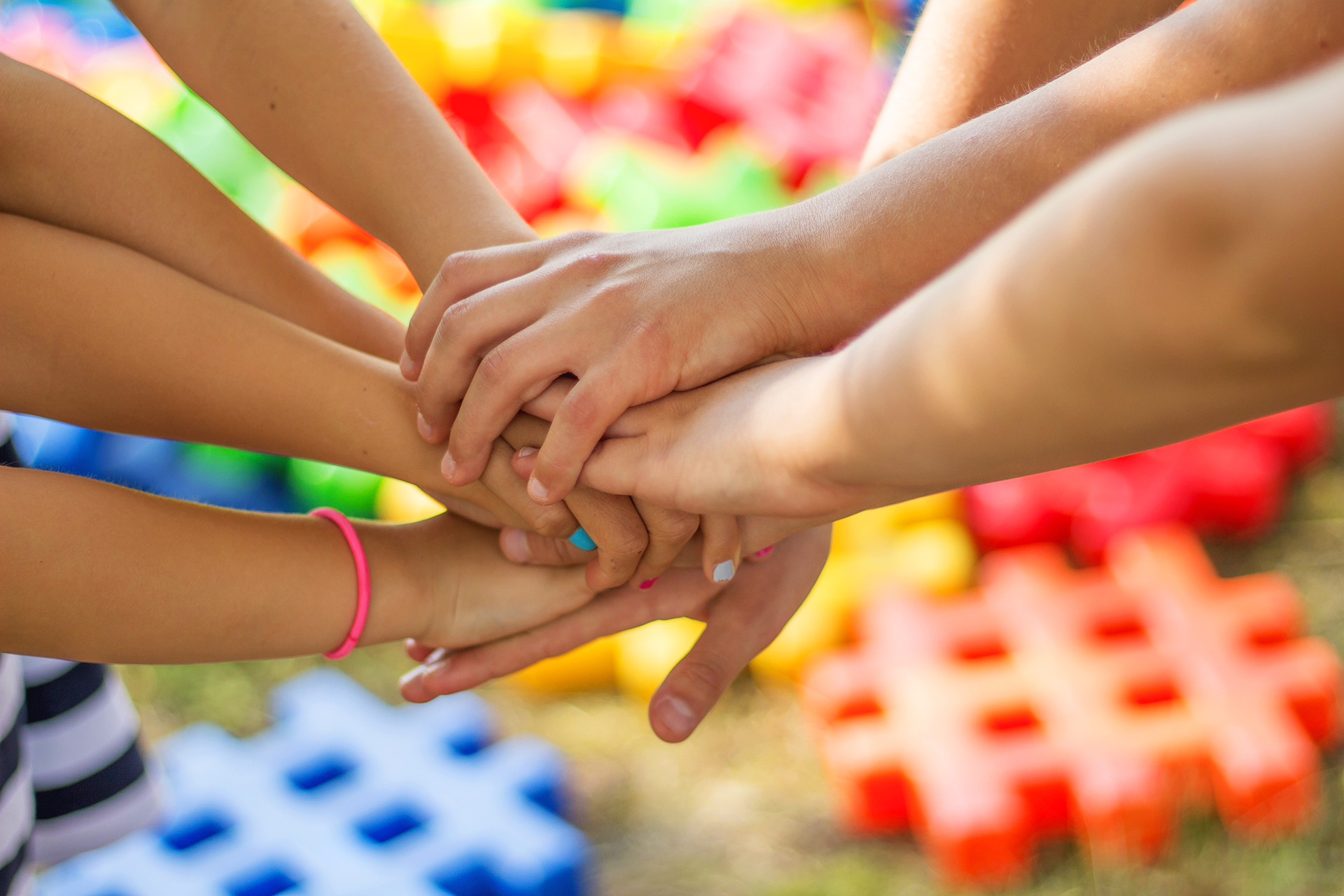 Viele Hände sind zusammengeklammert, symbolisierend für Einheit, Gemeinschaft und demokratisches Miteinander – im Hintergrund bunte Spielbausteine, die auf Projekte für Kinder und Jugendliche verweisen.