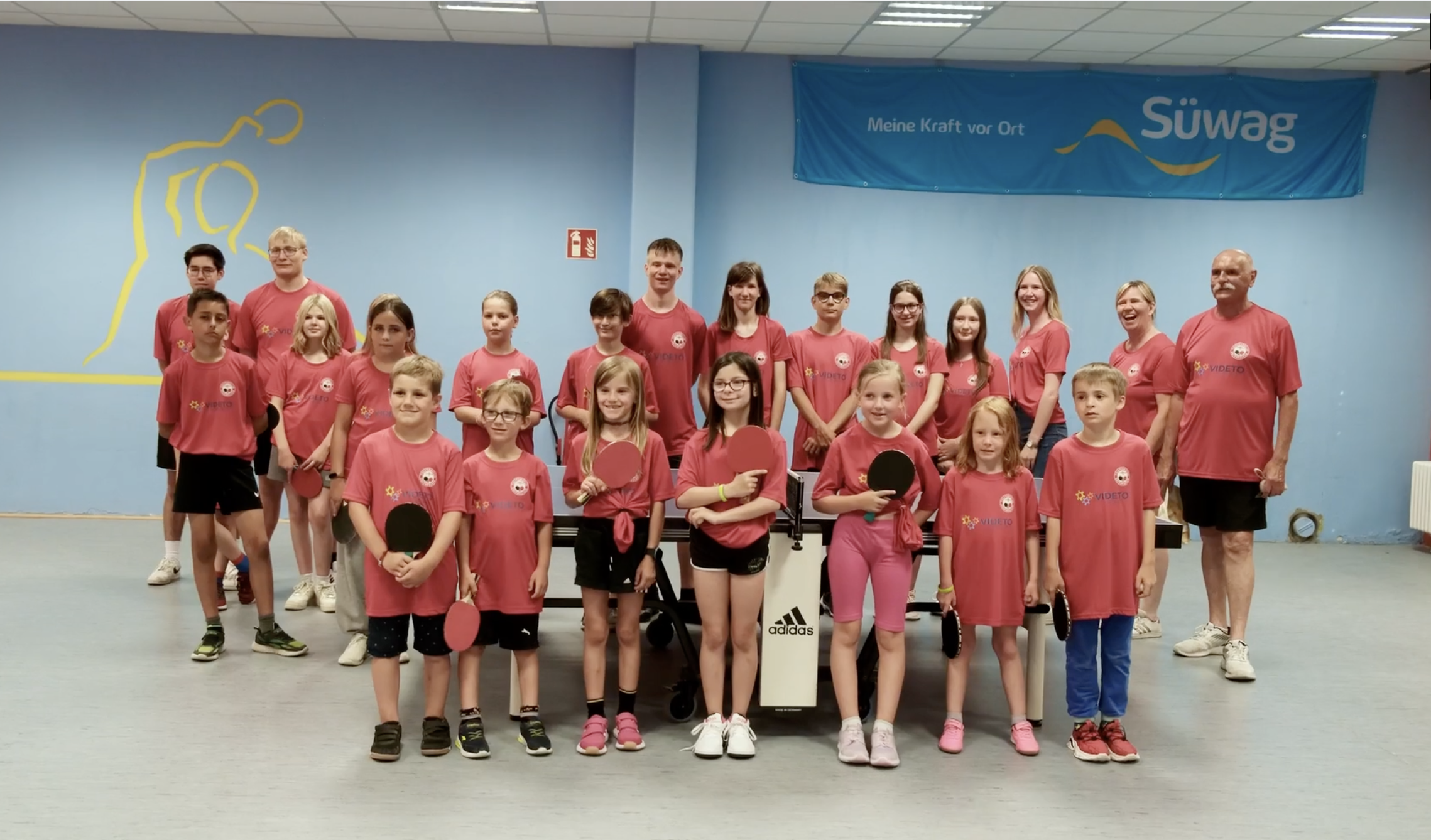 Gruppenfoto von Kindern und Erwachsenen in pinken VIDETO-T-Shirts bei einer Tischtennis-Aktion, unterstützt durch das Projekt VIDETO zur Förderung demokratischer Werte und respektvollem Miteinander.