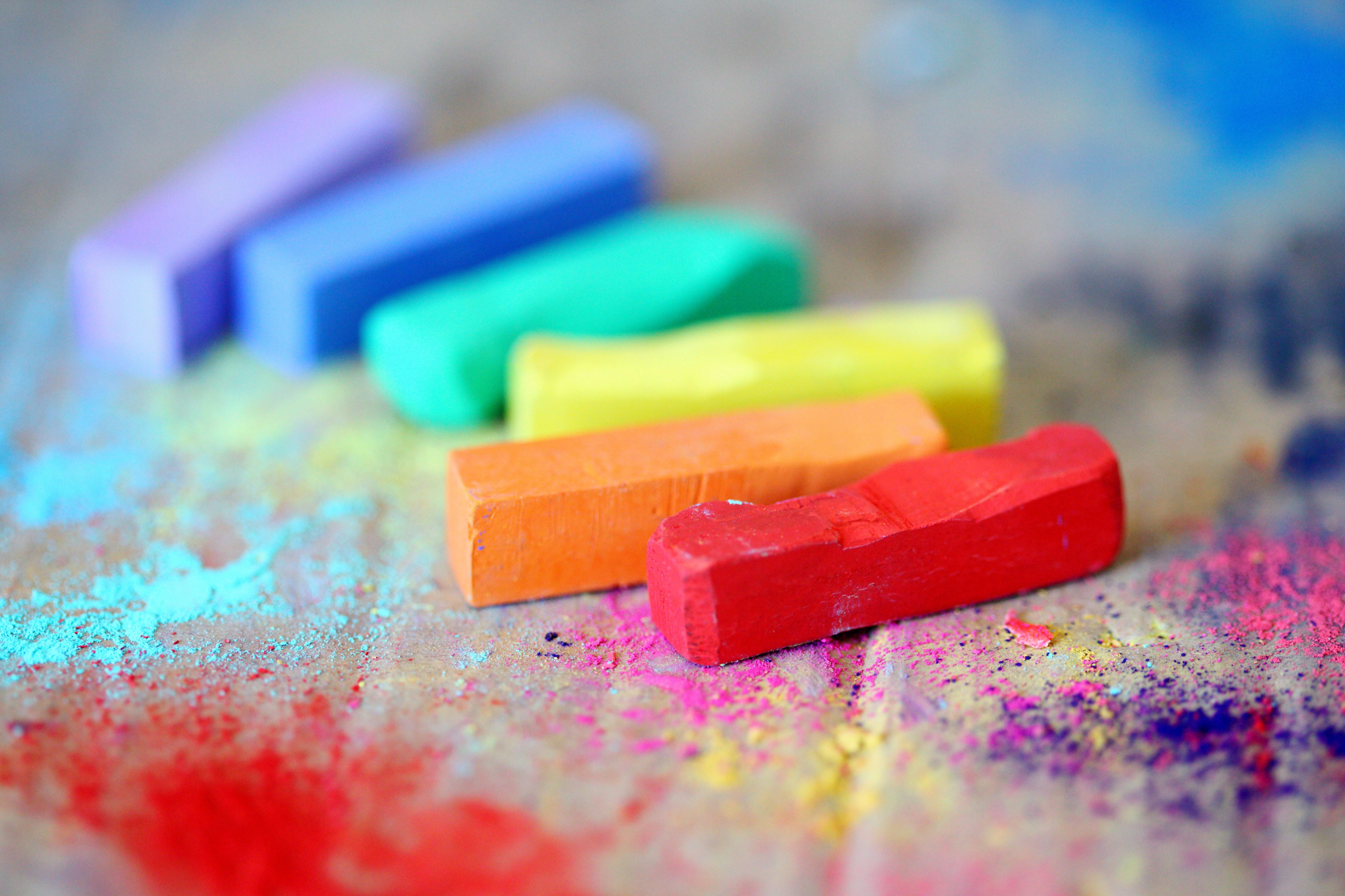 Bunte Kreidestifte in Regenbogenfarben (Rot, Orange, Gelb, Grün, Blau, Lila) liegen auf einer mit Farbpulver bestäubten Oberfläche, symbolisierend Vielfalt und kreative Ausdruck, die demokratische Werte wie Toleranz und Respekt stärken.