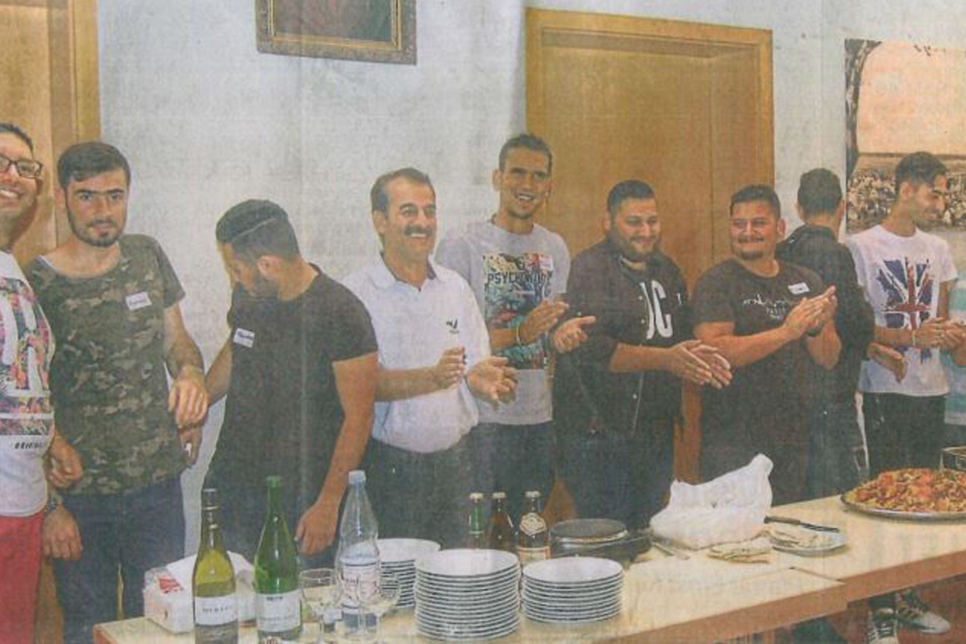 Gruppe von Männern bei einem gemeinsamen Kochen-Event zur Förderung sozialer Integration und respektvolles Miteinanders, mit Pizza und Getränken auf dem Tisch.