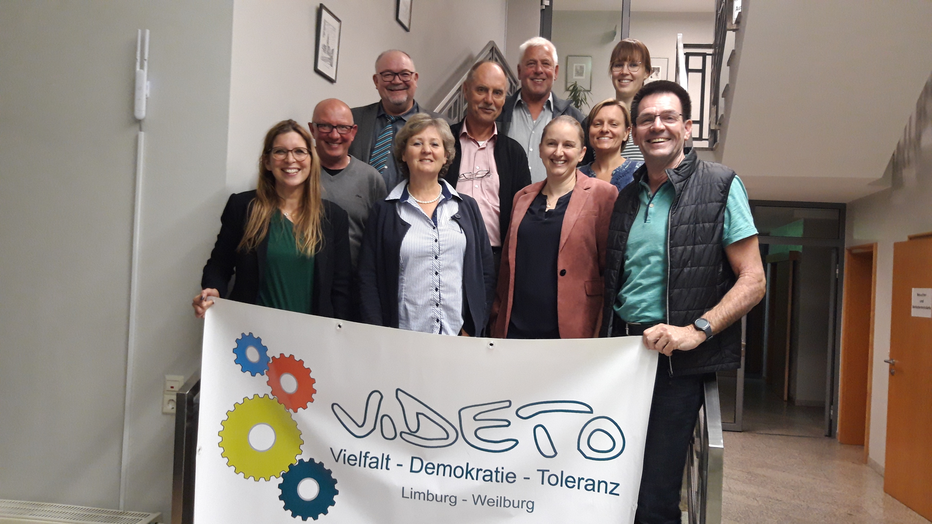 Ein Gruppenfoto von Mitgliedern des VIDETO-Begleitausschusses, die ein Banner mit dem Logo 'VIDETO' und den Werten 'Vielfalt - Demokratie - Toleranz' für die Region Limburg-Weilburg halten.