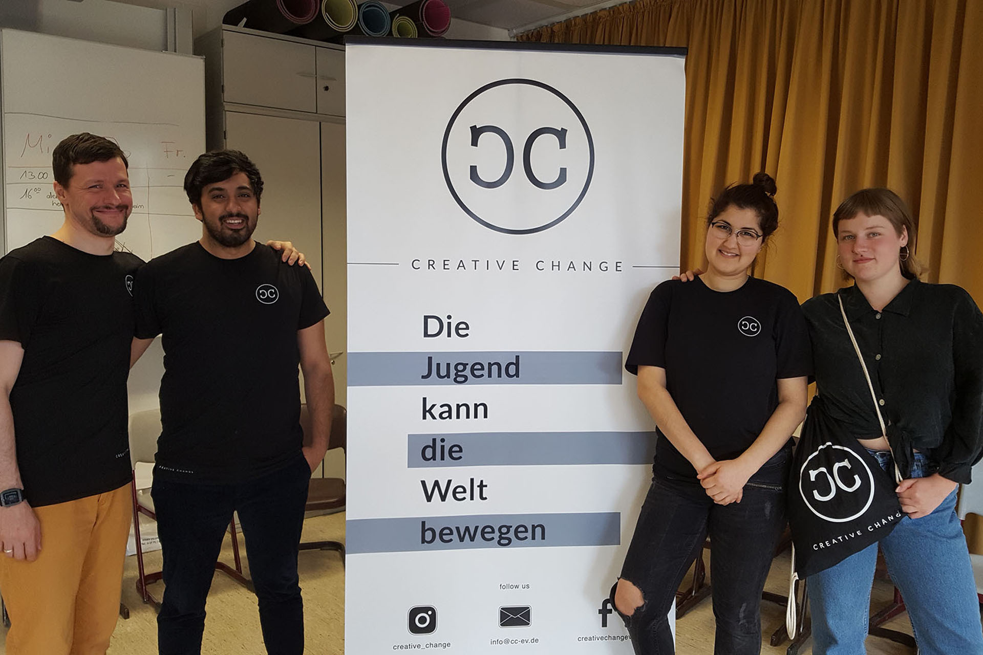 Vier Personen in schwarzen „Creative Change“-Shirts stehen vor einem Banner mit der Botschaft „Die Jugend kann die Welt bewegen“ – Teil eines VIDETO-Projekts zur Förderung demokratischen Engagements und des Abbau von Vorurteilen.
